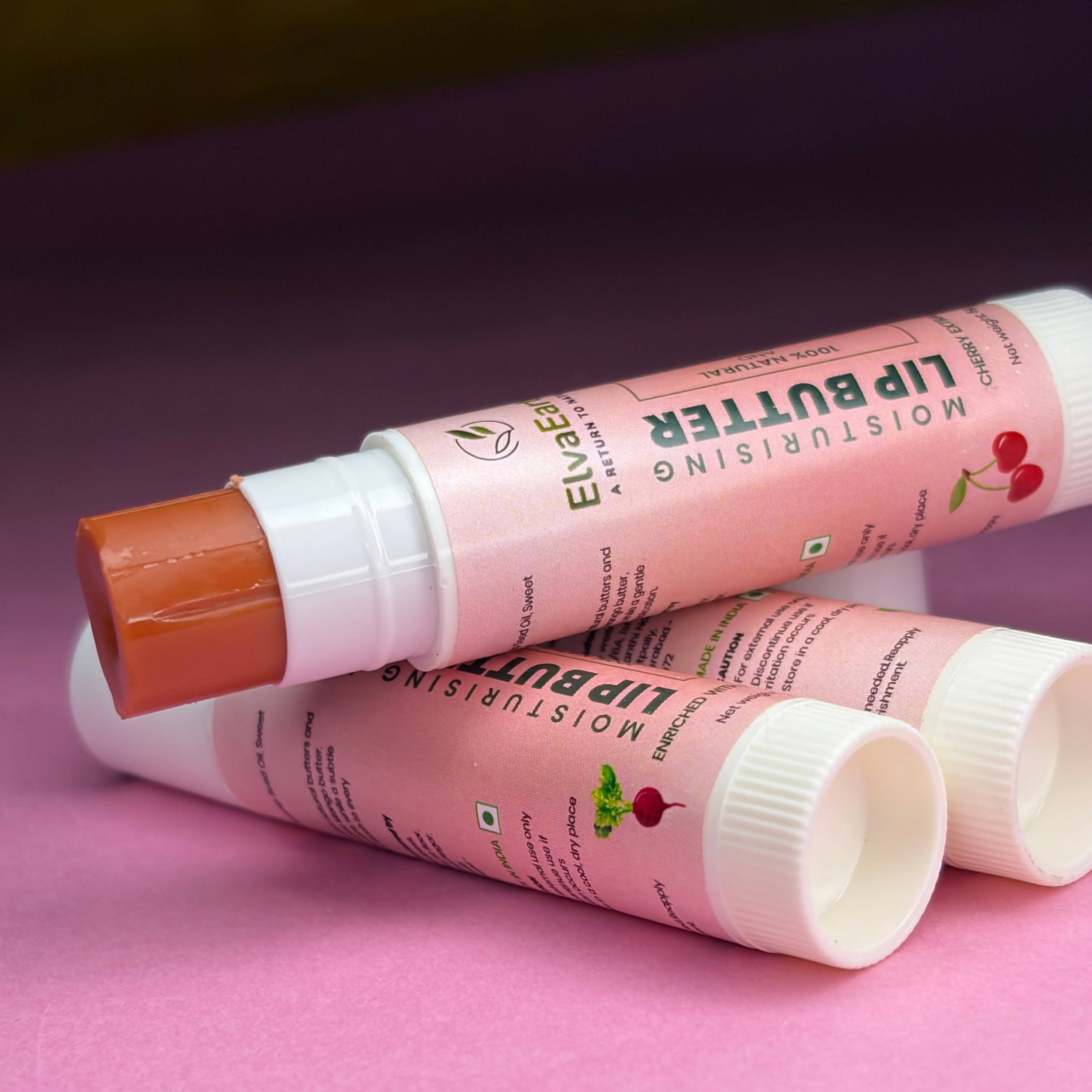 Three lip balm tubes with visible branding on a pink surface