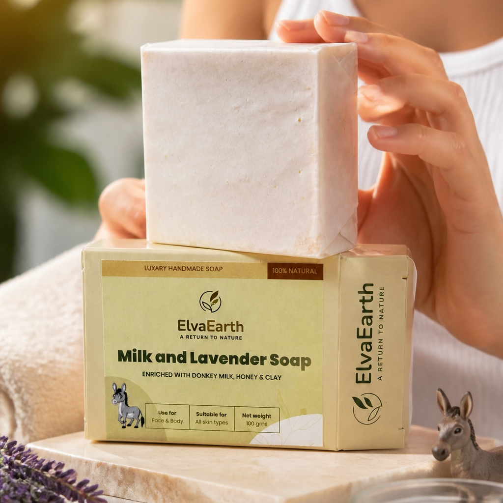 A person holds a rectangular bar of soap stacked on top of its branded box in a softly lit indoor setting. The product is ElvaEarth Milk and Lavender Soap, shown with the soap bar and packaging in warm beige, cream, and pale lavender tones.