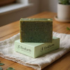 Green soap bar on a white box with 'ElvaEarth' branding, placed on a wooden surface with a plant in the background.