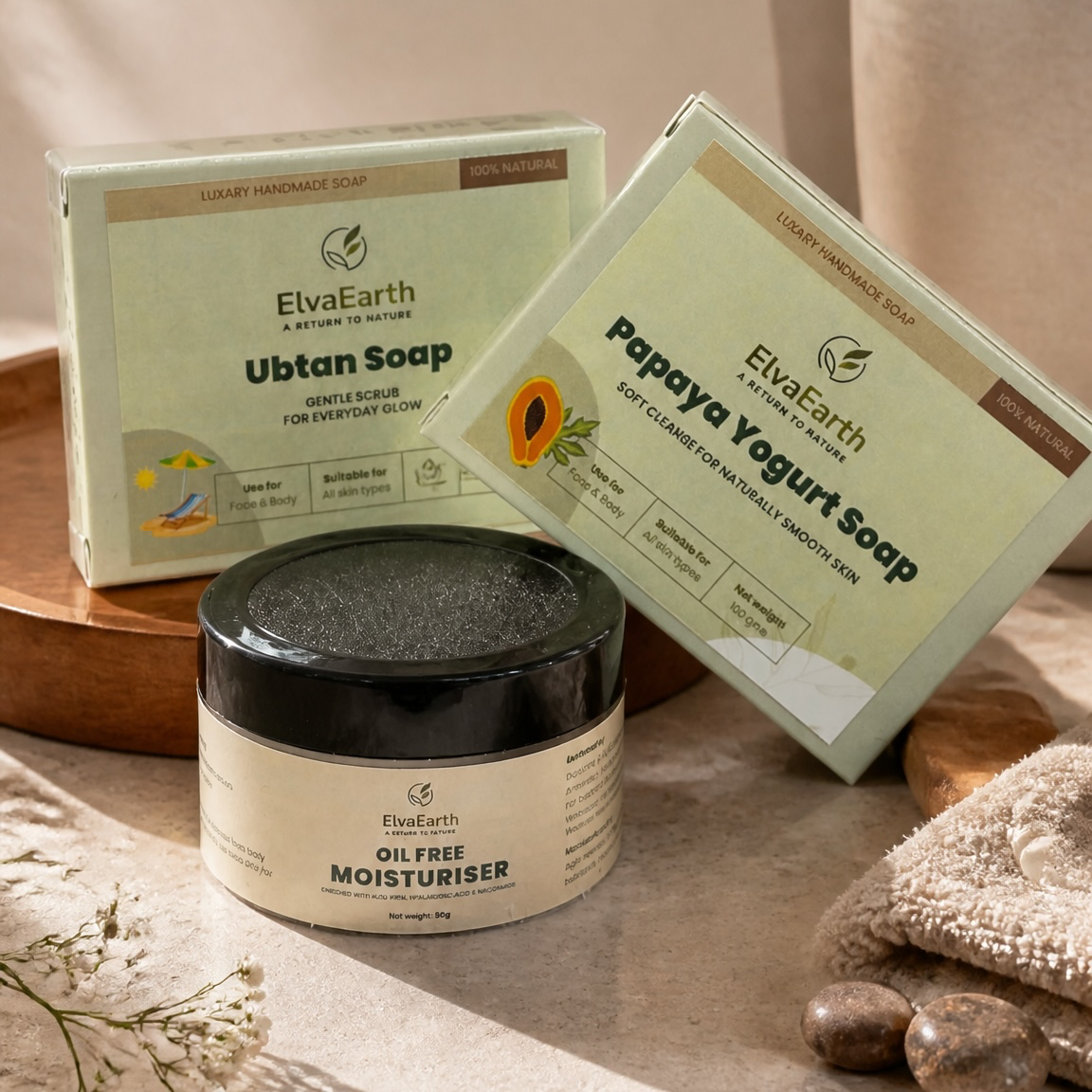 Three ElvaEarth skincare products arranged on a stone surface with a vase of greenery in the background: a jar of oil-free moisturizer in front, with two boxed soaps behind it labeled Ubtan Soap and Papaya Yogurt Soap. Text on the image reads 'Nature's Touch, Everyday Glow.